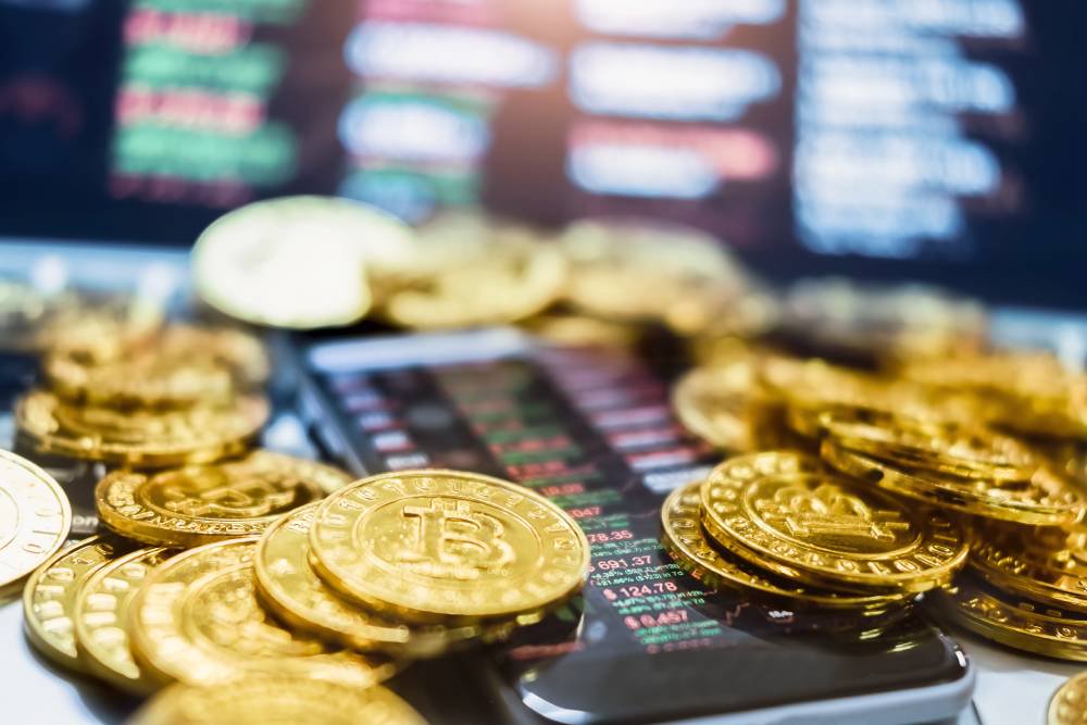 Физические сувенирные монеты биткоина лежат на мобильном телефоне с графиком котировок.