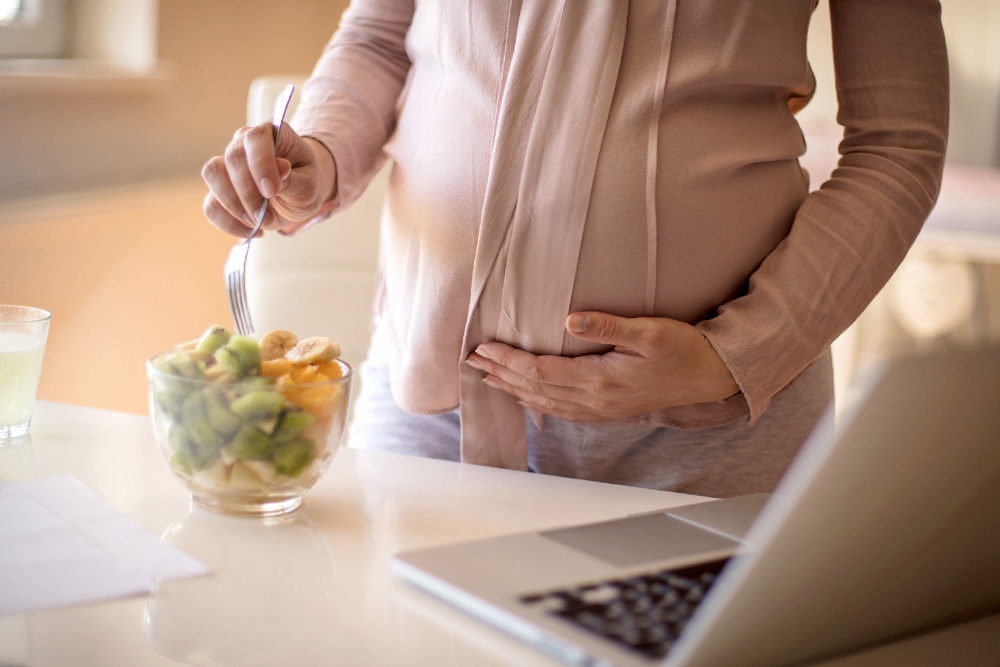 беременная женщина перемешивает фруктовый салат в миске