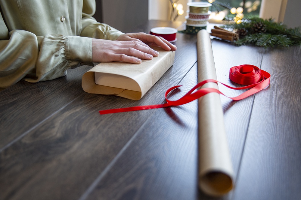 Девушка упаковывает книгу в подарочную бумагу.