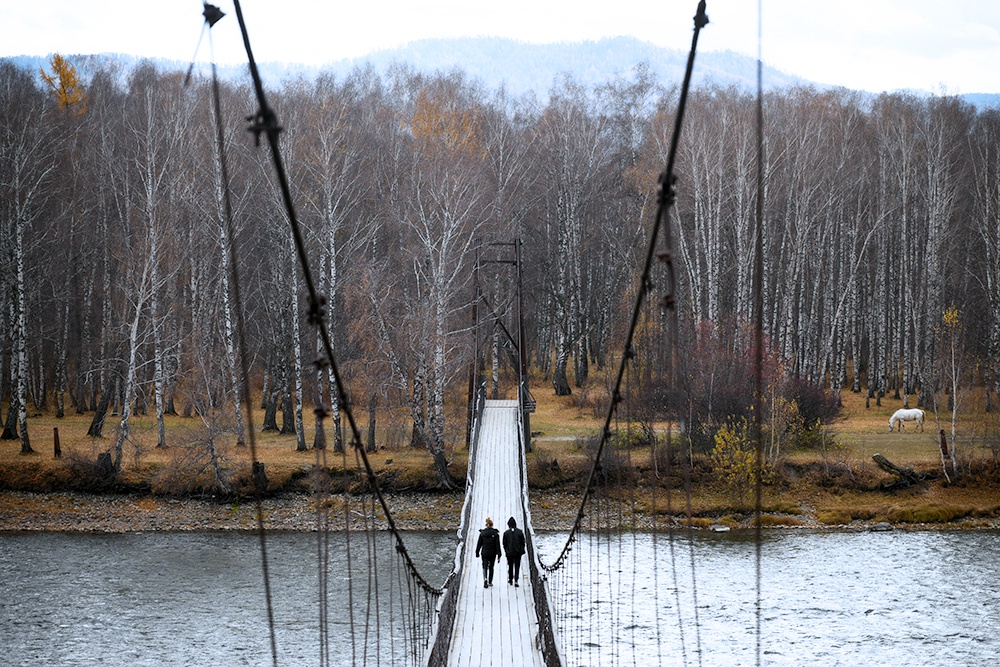 Два человека идут по пешеходному мосту через реку