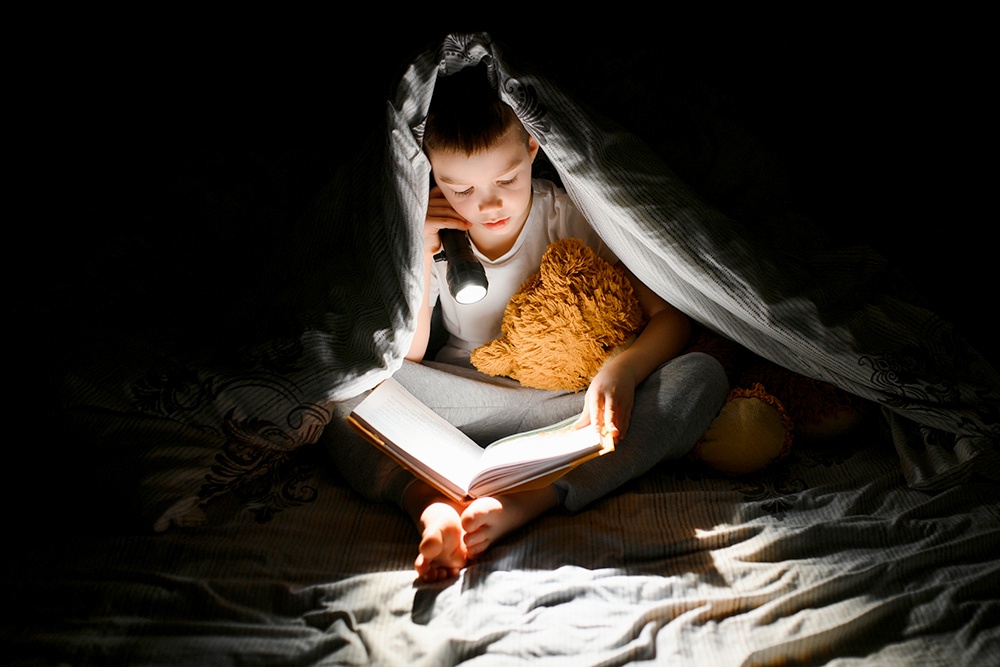 ребенок под одеялом читает книгу