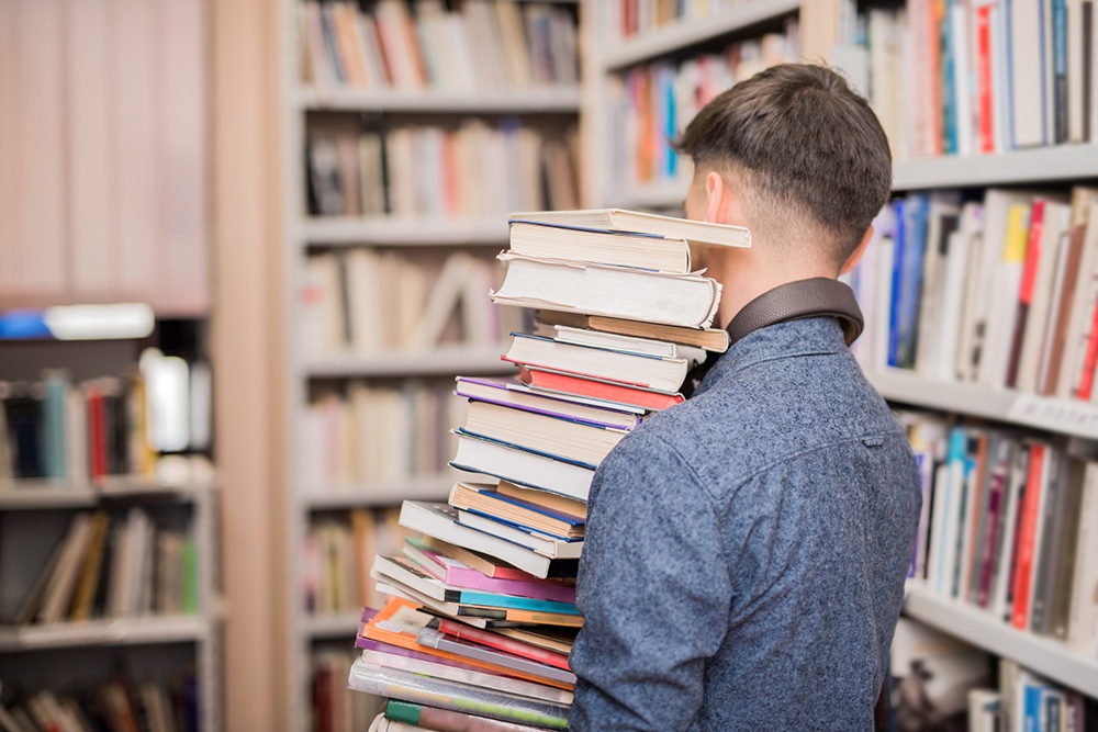 юноша несет стопку книг