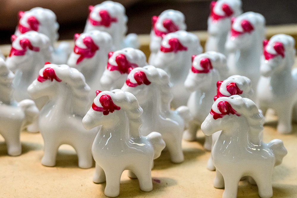 Множество керамических белых лошадок с ярко-розовой сбруей на голове.