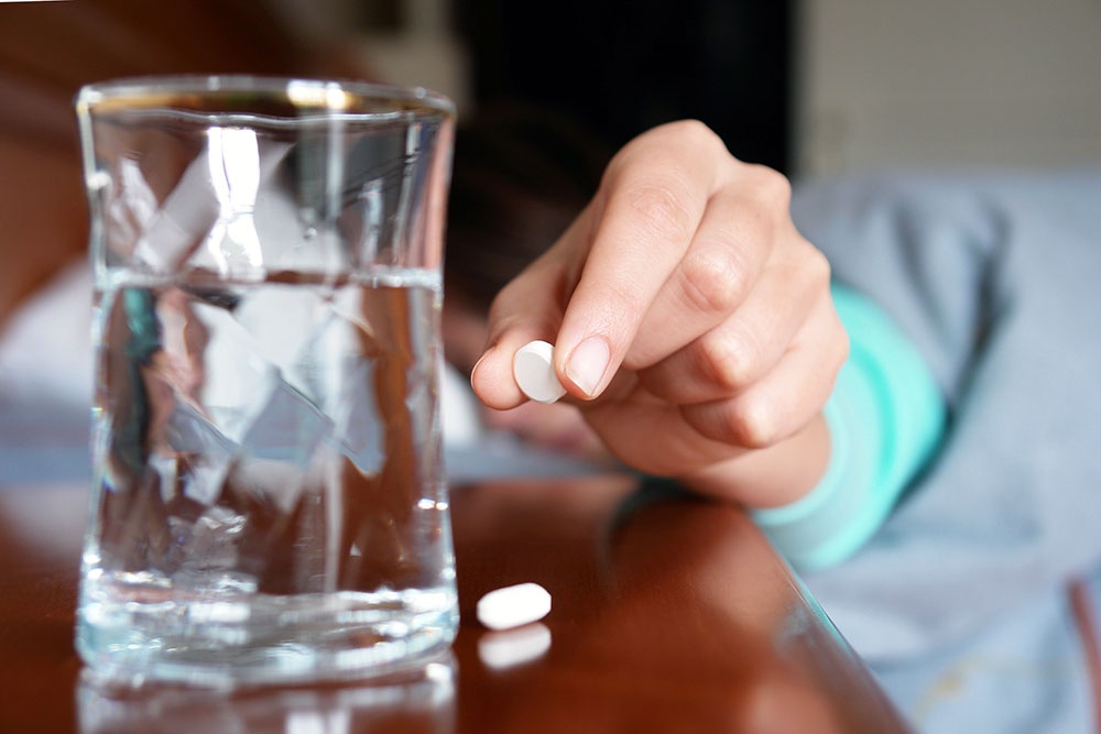 рука тянется за таблеткой и стаканом воды