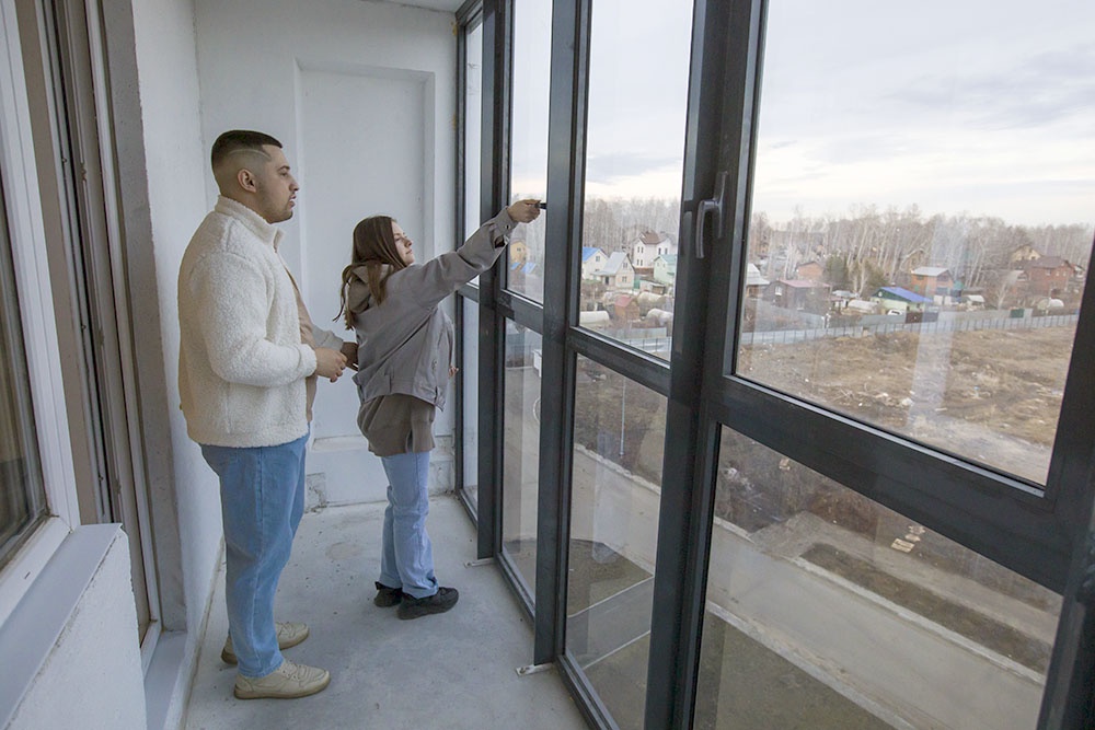 Женщина открывает окно на балконе в новостройке