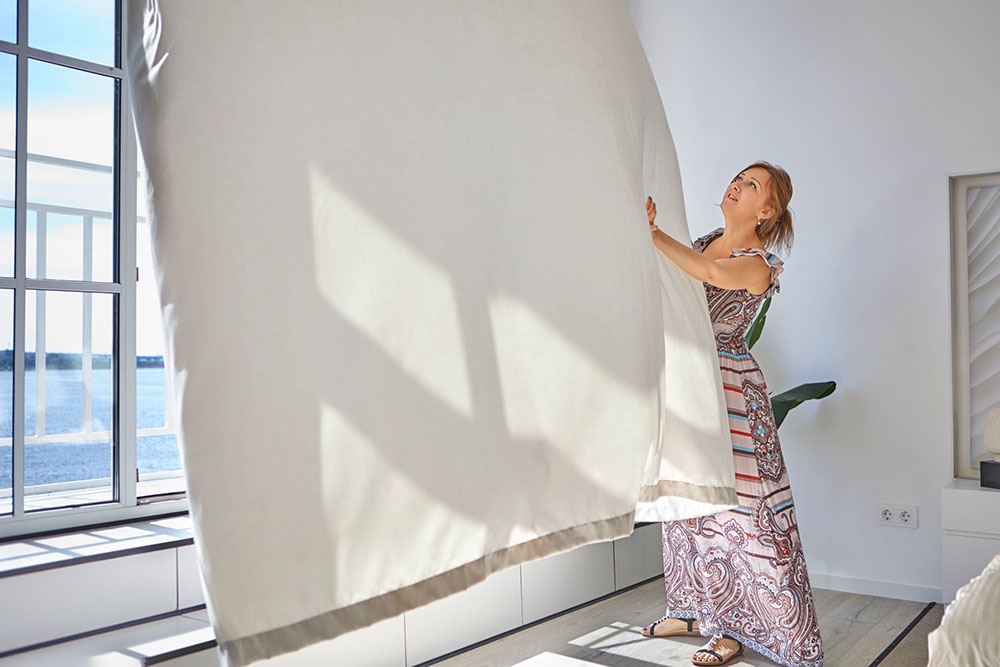 женщина поправляет штору возле открытого окна