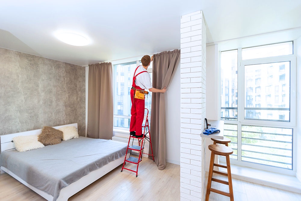 рабочий стоит на лестнице и вешает шторы в спальне