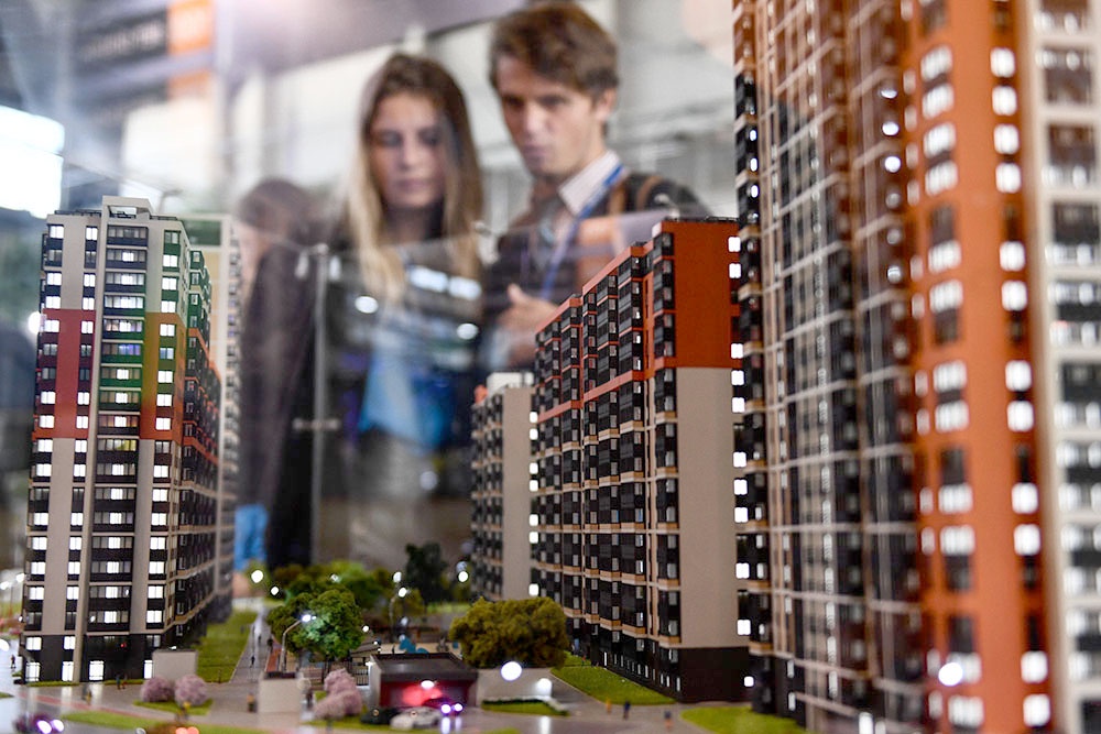 Молодая пара, мужчина и женщина рассматривают макет строящегося современного квартала в офисе застройщика