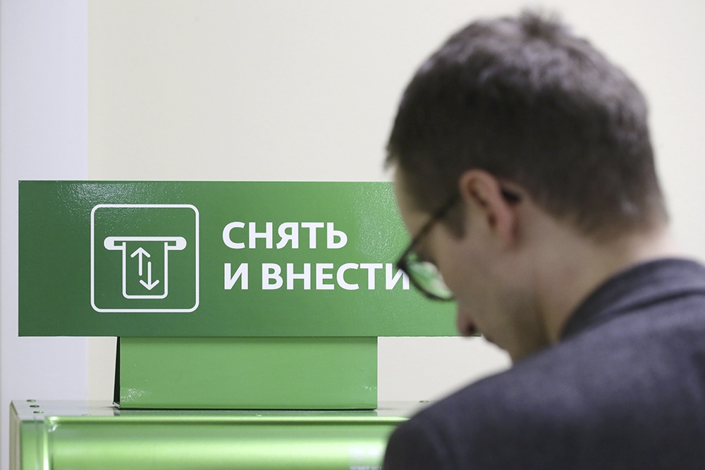 Человек стоит у банкомата, на банкомате вывеска "Снять и внести наличные"