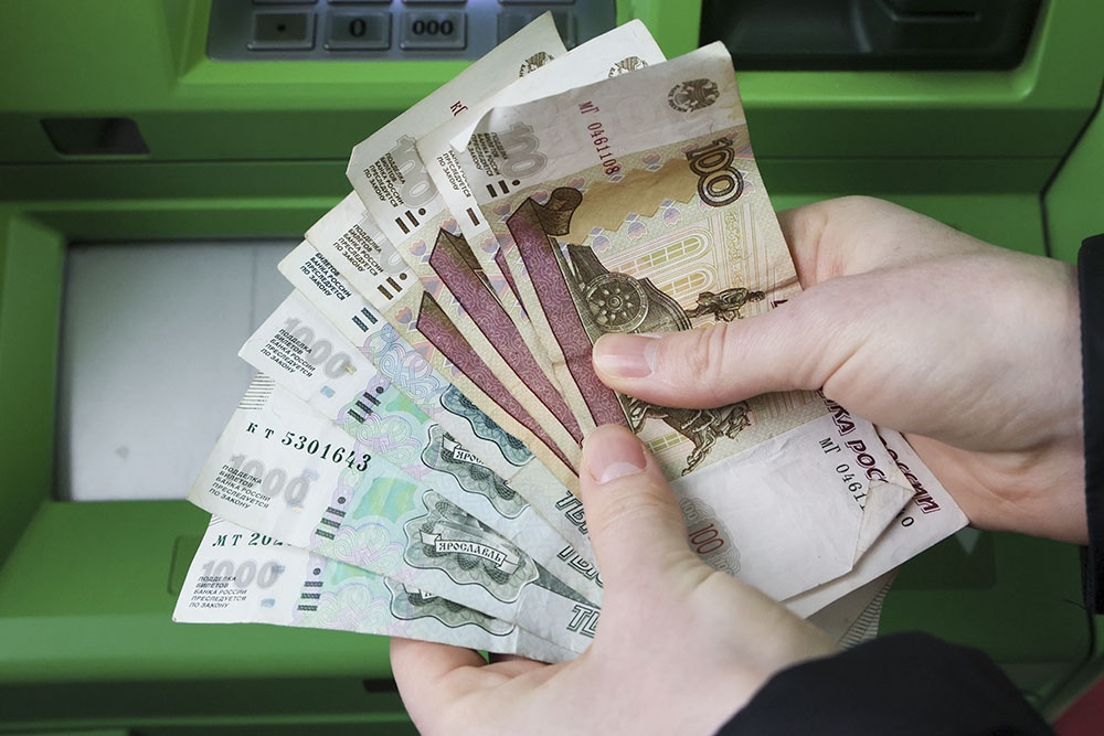 Человек подсчитывает купюры на фоне банкомата