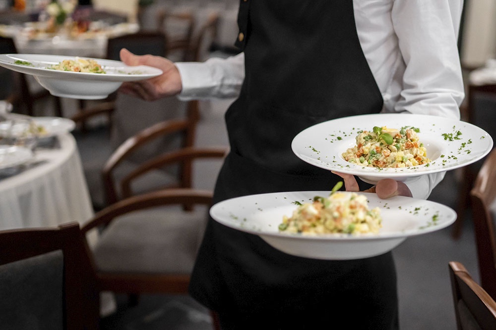 официант несет посетителям тарелки с салатом оливье