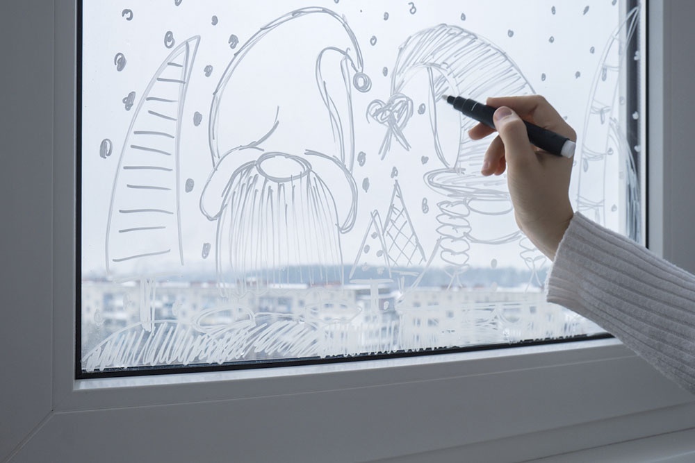 Человек рисует на окне новогодний декор