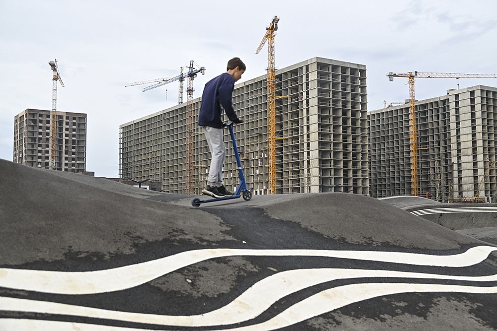 Юноша катается на самокате на фоне строительства нового современного жилого квартала