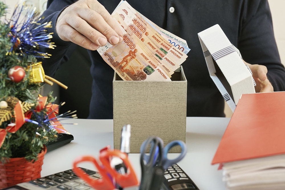 Человек складывает деньги в подарочную коробку