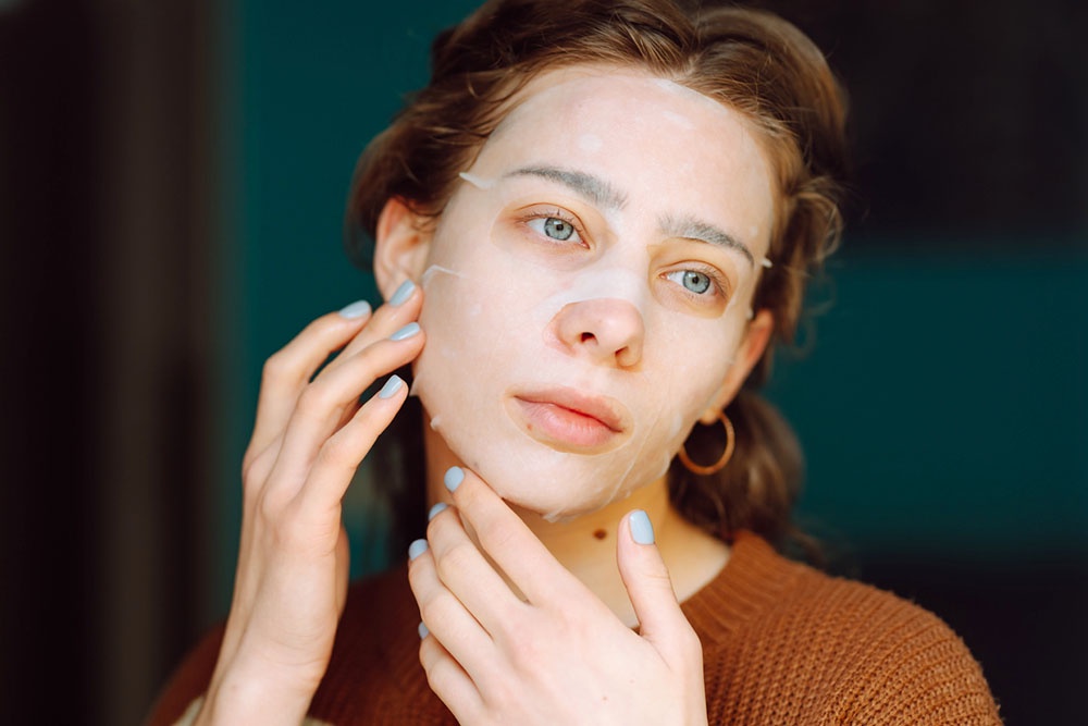 женщина наносит тканевую косметическую маску на лицо