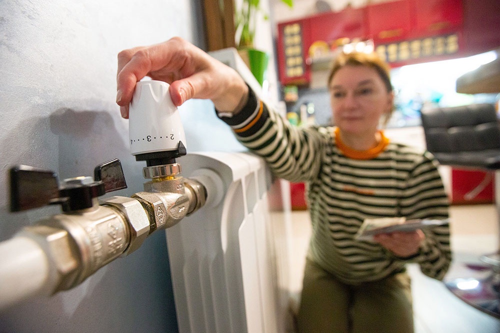 Женщина регулирует термодатчик на отопительной батарее