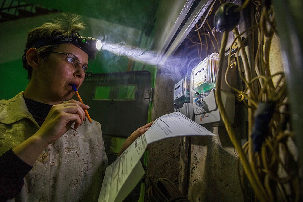 Женщина проверяет в темноте счётчики электроэнергии 