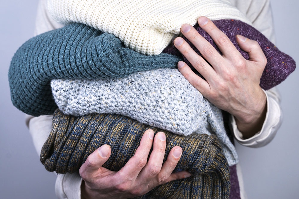 Мужчина держит в руках стопку свитеров