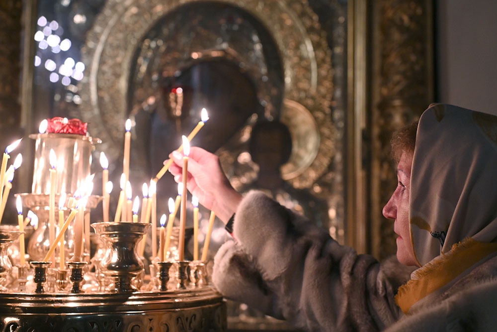 Верующая ставит свечу во время службы в канун праздника Крещения Господня в Богоявленском кафедральном соборе