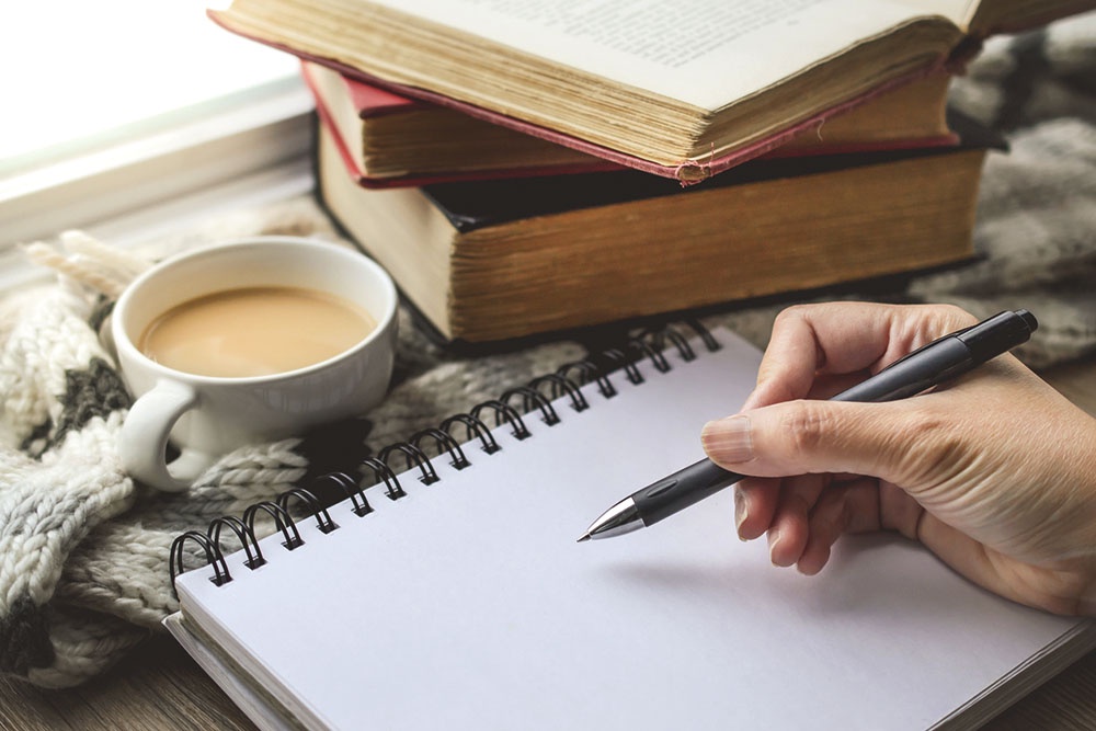 Стопка книги и человек пишет заметку в читательский дневник
