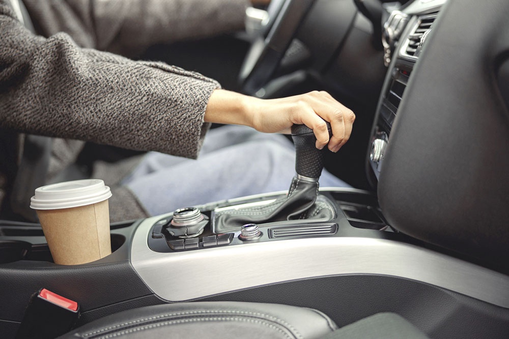 Девушка в автомобиле переключает коробку передач.