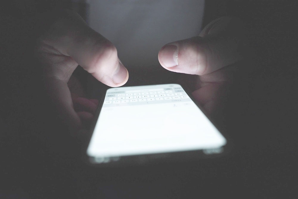 Человек набирает сообщение на смартфоне в темноте.