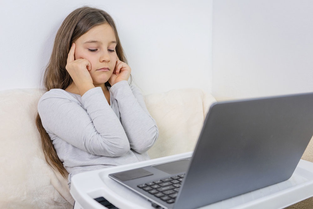 Девочка смотрит в экран компьютера, устала от информации