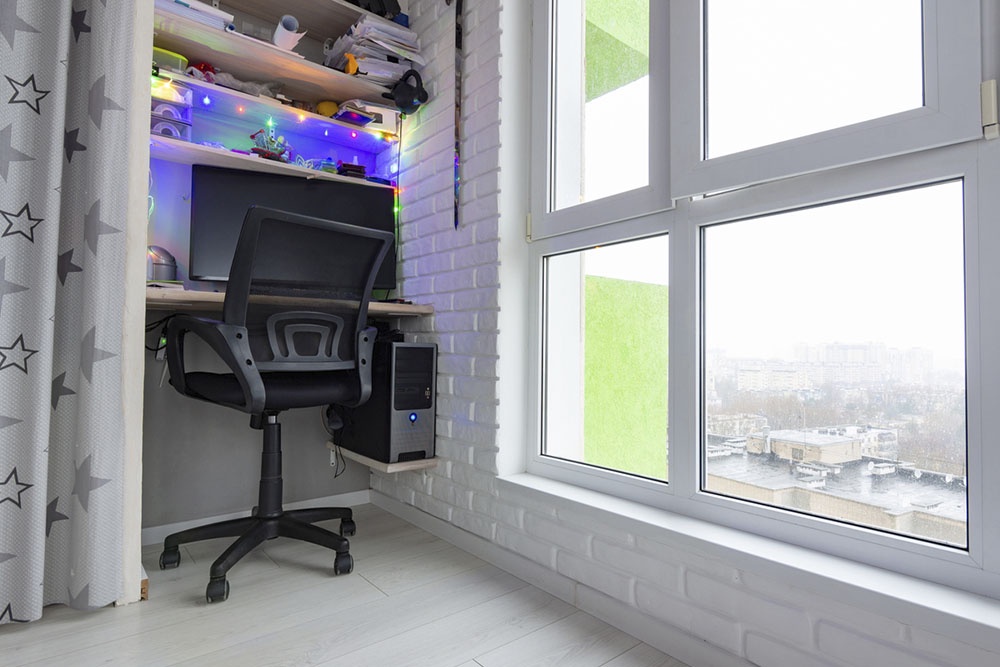 Утепленная и остекленная лоджия, превращенная в рабочий кабинет с компактным столом, стеллажом и полками.