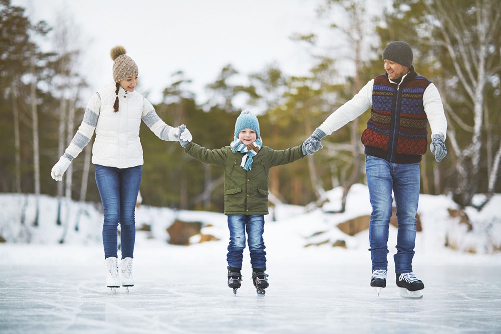 Семья на активной зимней прогулке в парке, родители и ребенок катаются на коньках. 