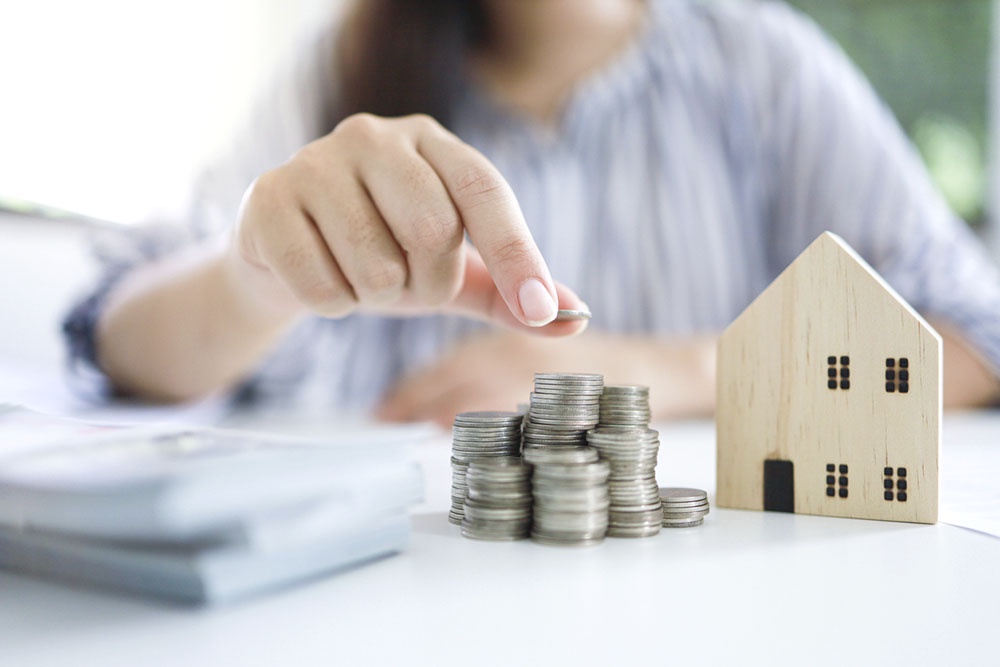 Рука кладет монеты в стопку, символизируя накопление первоначального взноса на ипотеку.