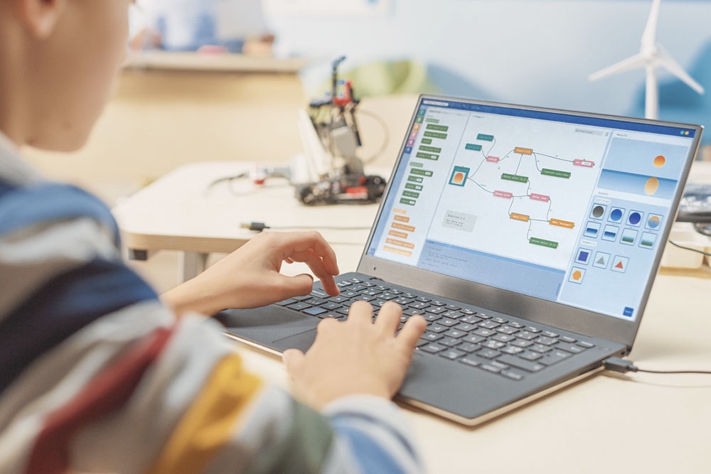 Школьник младших классов увлеченно работает за компьютером, изучая программирование в визуальной среде.