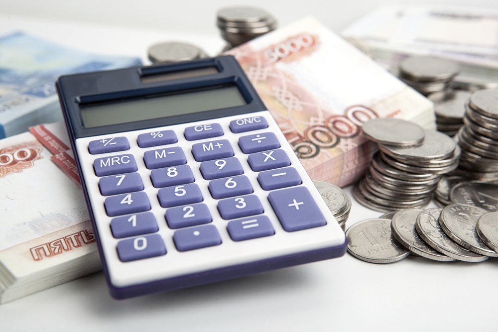 Стопка денег и калькулятор на столе, символизирующие расчет налогового вычета при покупке жилой недвижимости.