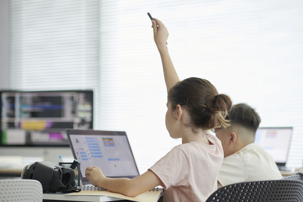 Ученица активно тянут руки, чтобы ответить, в компьютерном классе.