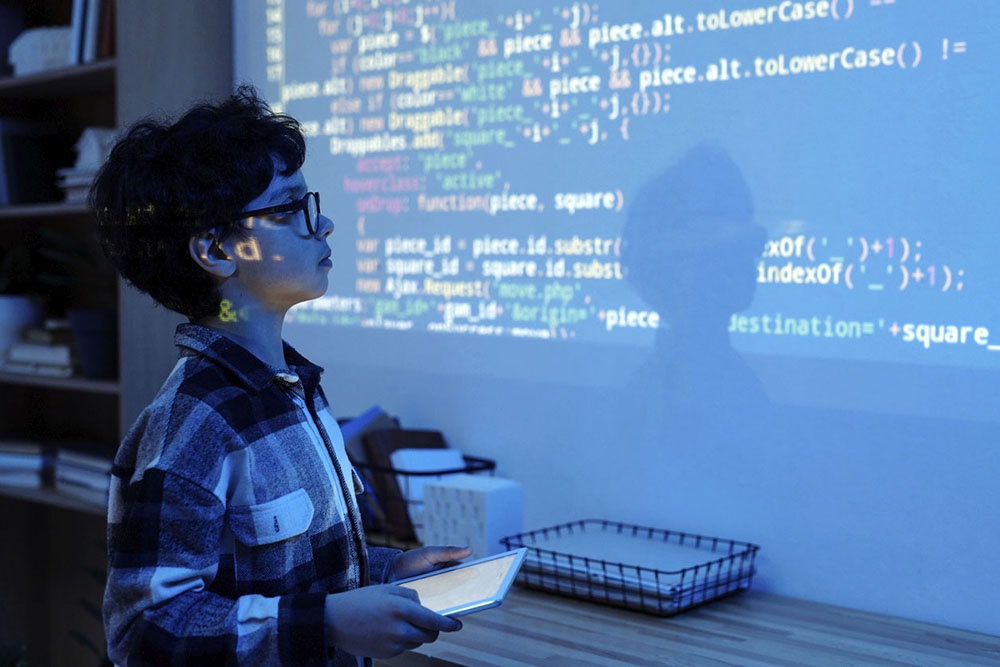 Мальчик занимается программированием, изучая код, проецируемый на стену или экран.