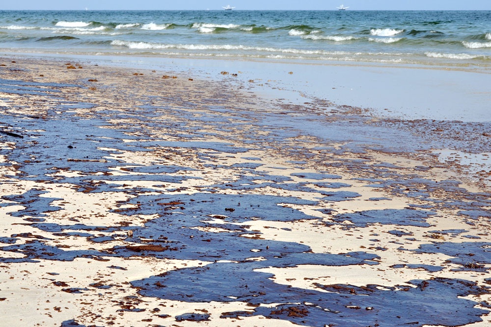 Масштабный разлив нефти песчаном берегу моря.