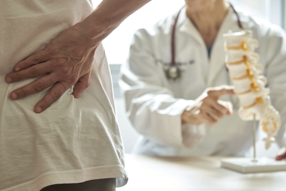 Пациент на приеме у врача показывает на больную спину во время консультации.