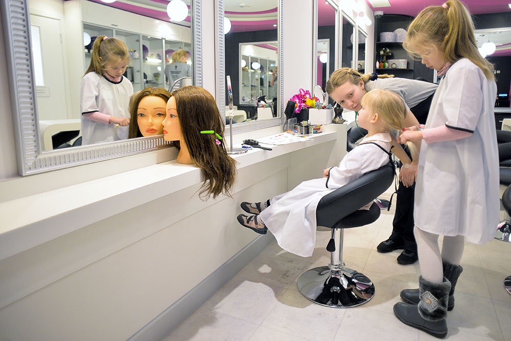 Дети в профессиональном салоне красоты "Кидзании": девочка делает прическу манекену, мальчик смотрит в зеркало.