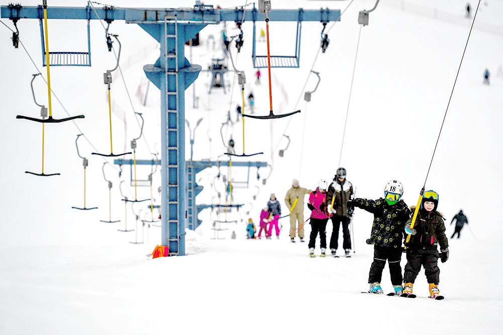 Дети в лыжных костюмах едут на бугельном подъемнике по склону спортивного парка "Волен".