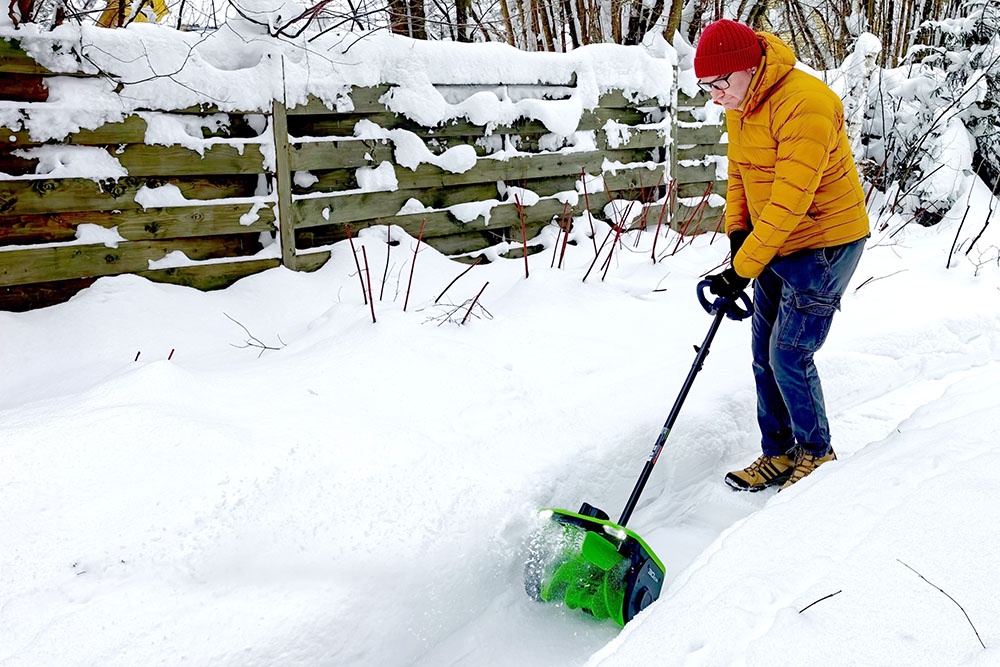 Человек управляет компактной электролопатой, расчищая дорожку от свежего снега.