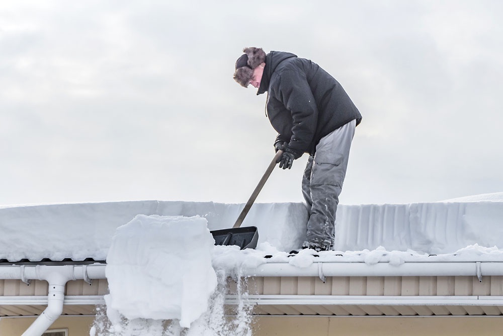 Мужчина чистит снег с крыши в одиночку.