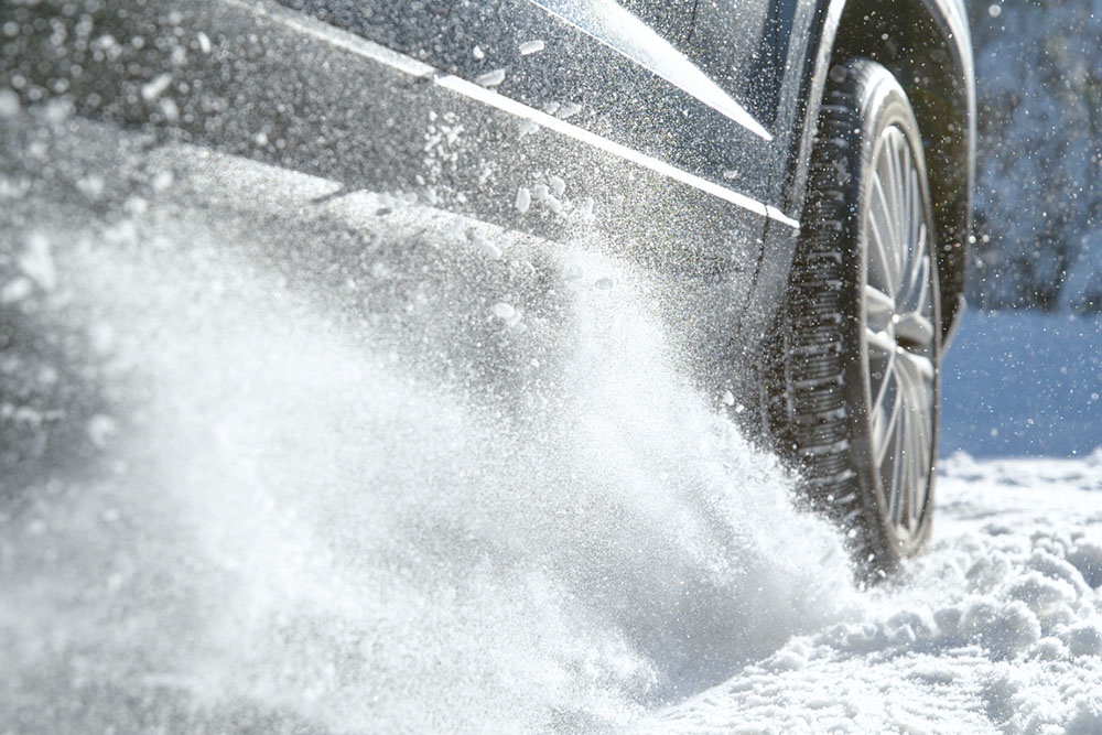 Бесполезная пробуксовка: колеса застрявшего автомобиля бешено вращаются в снегу, разбрасывая его, но машина не двигается.