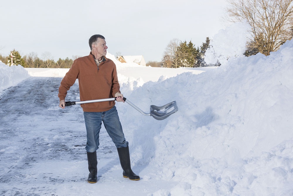 Человек убирает снег лопатой с изогнутой ручкой, спина остается в более прямом положении.