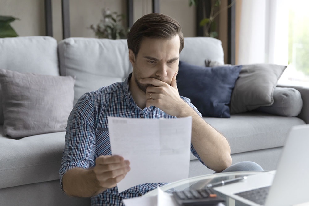 Мужчина задумчиво изучает документы, держит в руках договор ДДУ и смотрит на выписку с эскроу-счета.
