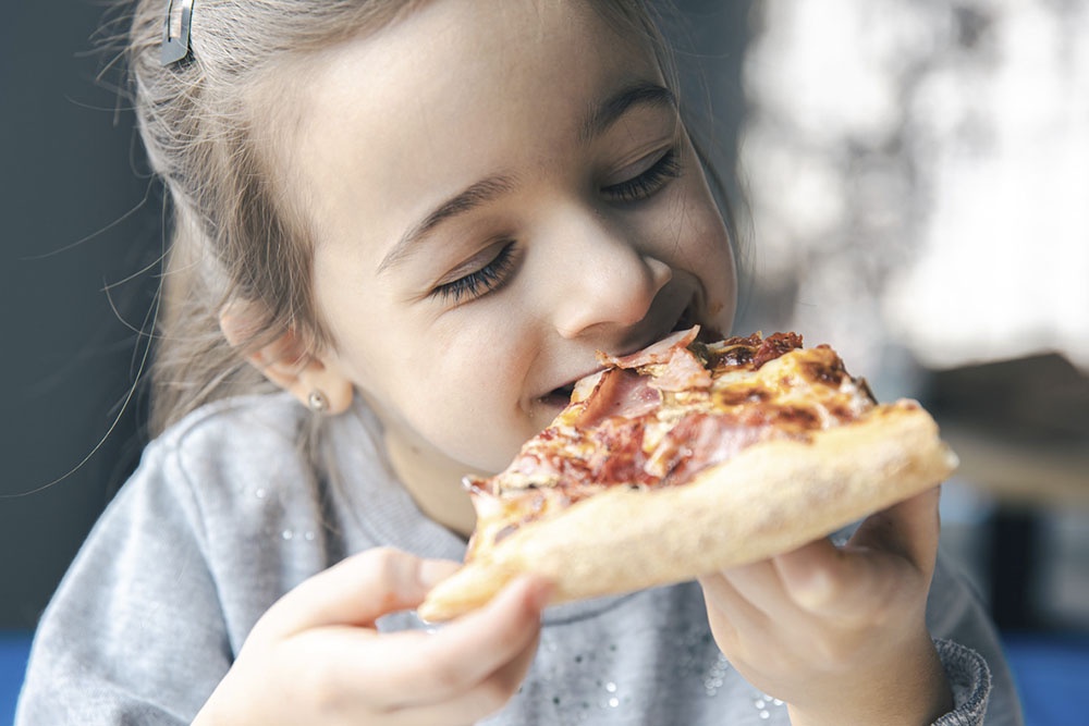 Крупный план лица ребенка, наслаждающегося вкусом любимой пиццы.