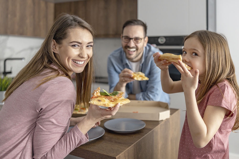 Семья за столом выбирают кусочки   пиццы, улыбаясь и общаясь.