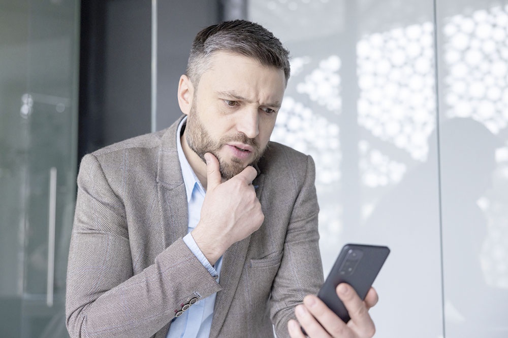 Мужчина сосредоточенно смотрит в экран смартфона, сидя в кресле или стоя на улице.