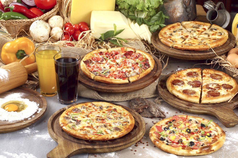 Ассорти из нескольких видов пиццы с разными начинками на одном большом столе.