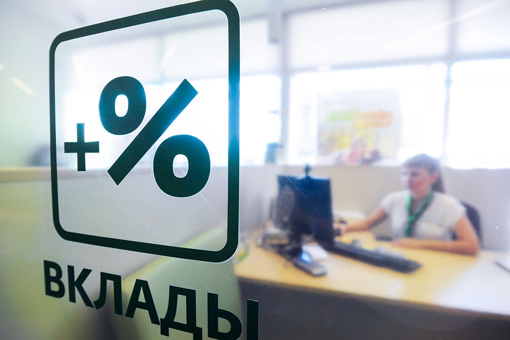 Сотрудник банка в рабочей обстановке, где видна табличка, указывающая на услуги по вкладам.