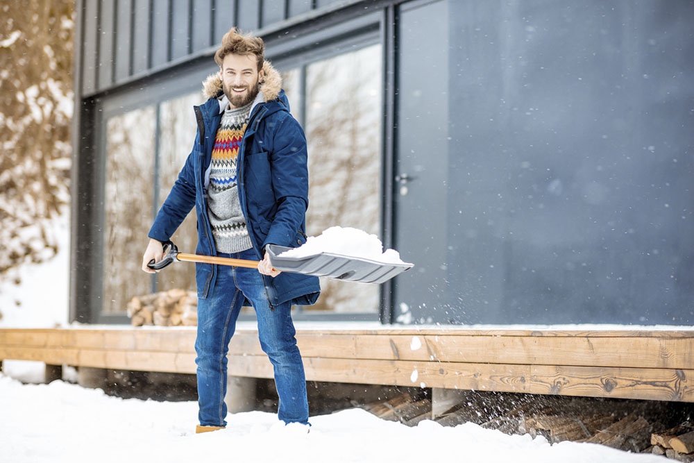 Владелец небольшого дачного участка убирает снег лопатой, не испытывая затруднений.