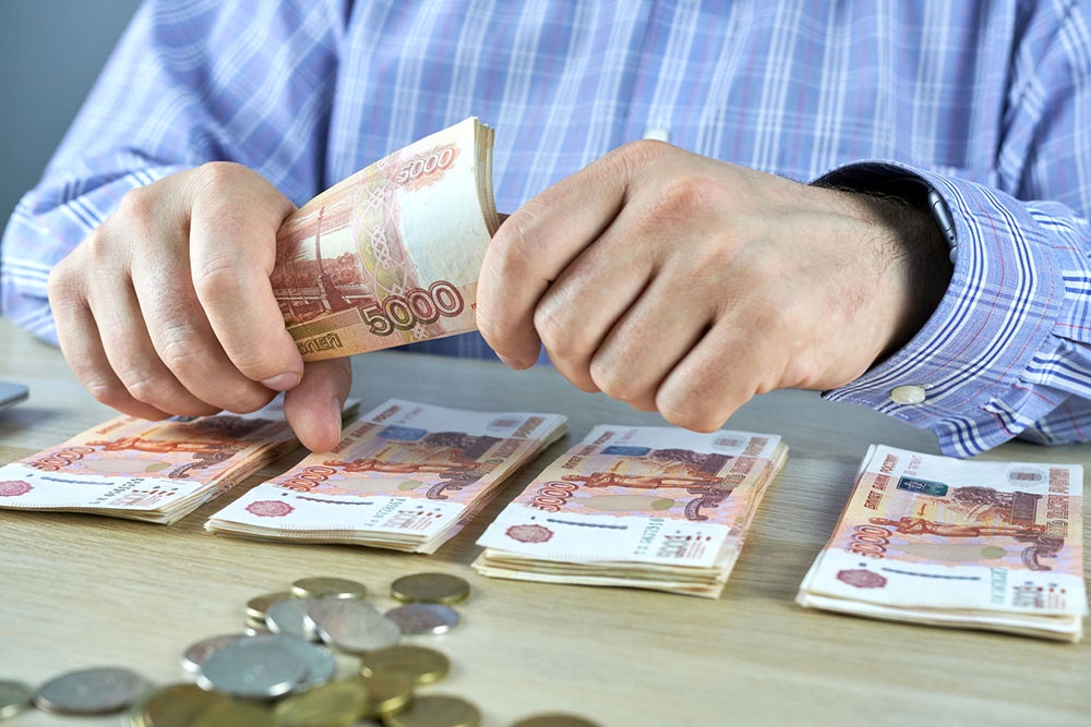 Человек пересчитывает и откладывает купюры.